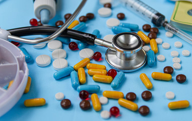 The concept of health and medicine.  Assorted pharmaceutical tablets, stethoscope and pill boxes on blue background.
