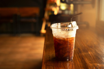 cold ice take coffee drink glass with plastic straw on wood counter table bar in cafe with soft...