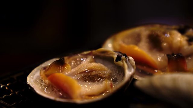 4K Close up shot of grilled hard clam shellfish on charcoal grill stove. Grilled seafood in japanese seafood restaurant.