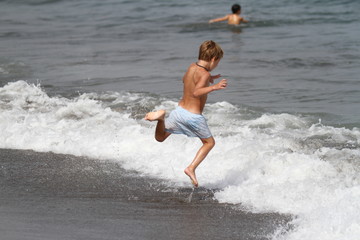 Little boy playing with waves on the beach 