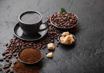 Cup of fresh raw organic coffee with beans and ground powder with cane sugar cubes with coffee tree leaf on black background. Top view