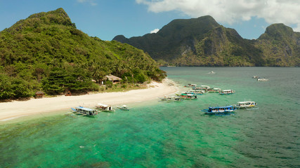 aerial view tropical beach on island with palm trees, blue lagoon and azure clear water. tourist boats on coast tropical island. Helicopter Island in El Nido, Palawan Philippines. Tropical landscape