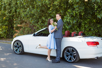 Romantic wedding couple standing in front of cabriolet car, beautiful happy bride and groom in...