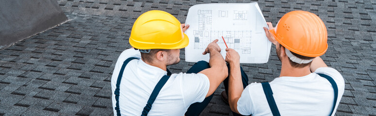 panoramic shot of builders in helmets looking at blueprint