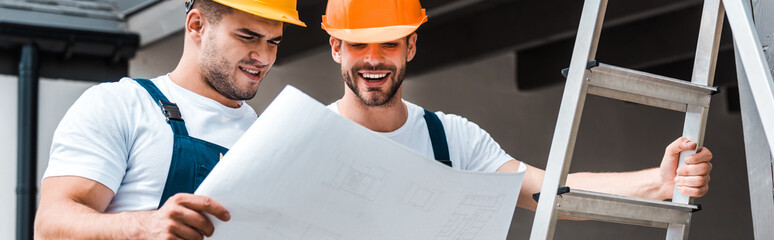 panoramic shot of happy builders in helmets looking at paper