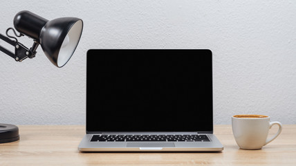 Open laptop screen on a desktop with a cup of coffee on a white wall background.Mockup.