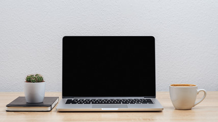 A blank laptop screen on an office desk with various items, on a white wall background.Mockup.