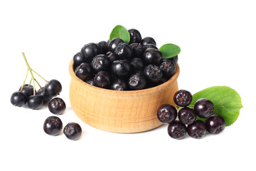 Chokeberry in wooden bowl with green leaves isolated on white background. Black aronia