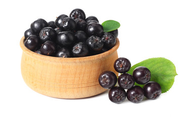 Chokeberry in wooden bowl with green leaves isolated on white background. Black aronia