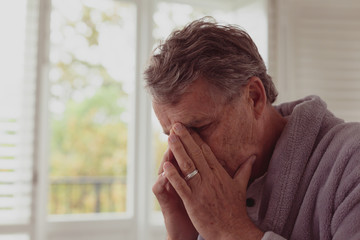 Sad active senior man with hands on face in a comfortable home