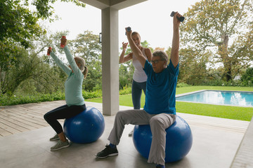 Female trainer assisting active senior couple to exercise with dumbbell in the porch