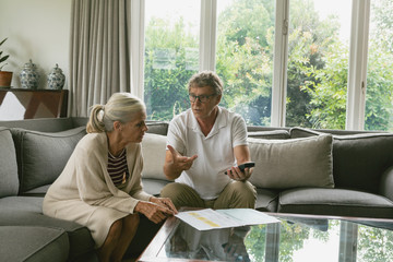 Obraz premium Active senior couple calculating domestic bills on sofa in living room