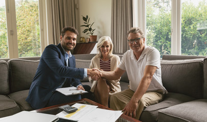 Active senior man shaking hands with real estate agent in living room - obrazy, fototapety, plakaty