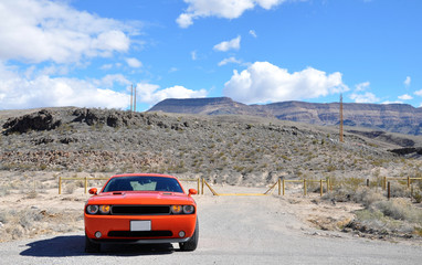 Fast red orange sport muscle car with burning lights in cloudy weather near mountains