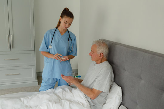 Female doctor giving medicine to active senior patient in bedroom