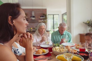 Multi-generation family praying before having food on dining table