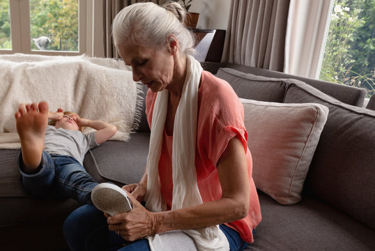 Grandmother removing shoes of her grandson on sofa in a comfortable home