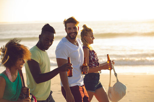 Group of friends holding beer bottles and walking together on the beach