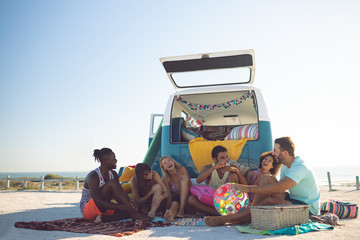Group of friends interacting with each other near camper van at beach