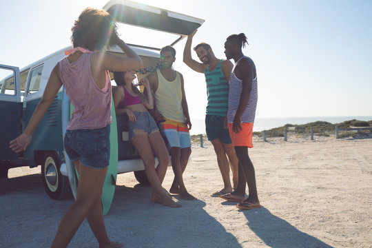 Group of friends interacting with each other near camper van at beach