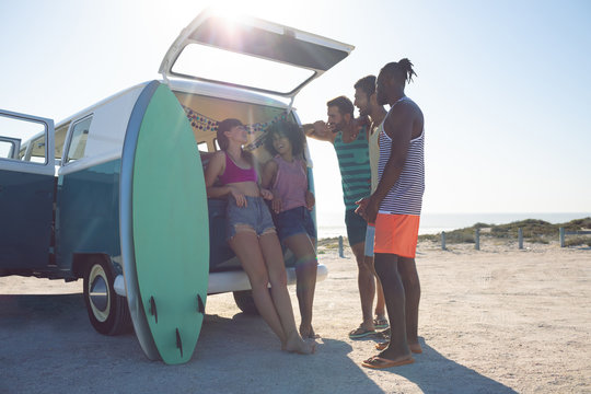 Group of friends interacting with each other near camper van at beach