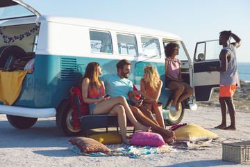 Group of friends interacting with each other near camper van at beach