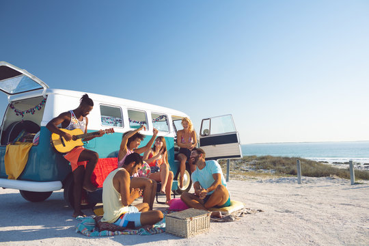Group of friends having fun near camper van at beach