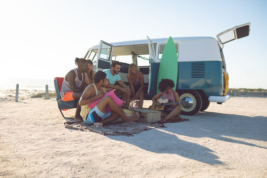 Group of friends having fun near camper van at beach