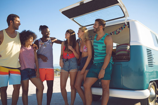 Group of friends interacting with each other near camper van at beach