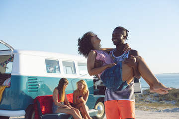 Man holding woman in his arms near camper van at beach