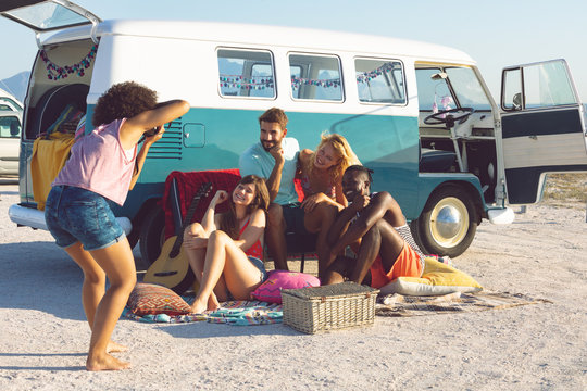 Woman taking pictures of her friends with digital camera near camper van at beach 
