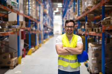 Portrait of middle aged warehouse worker standing in large warehouse distribution center with arms...