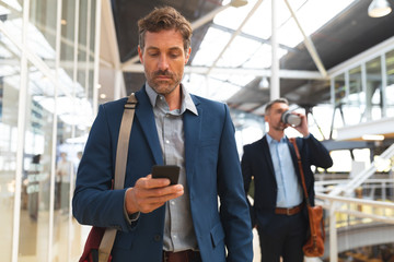 Businessman using mobile phone while walking in the corridor