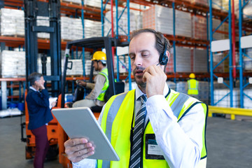 Male supervisor using digital tablet while talking on headset in warehouse