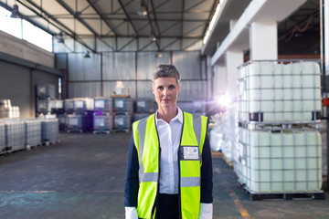 Fototapeta na wymiar Mature female staff in reflective jacket standing in warehouse