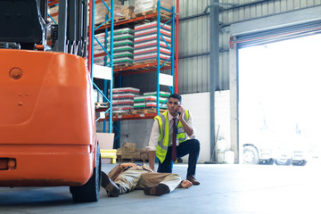 Male supervisor talking on mobile phone while his coworker lying unconscious on the floor