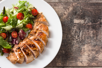 Grilled chicken breast with vegetables on a plate on wooden table. Top view. Copyspace