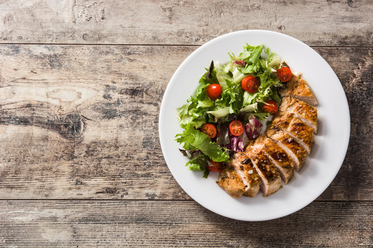 Grilled chicken breast with vegetables on a plate on wooden table. Top view. Copyspace
