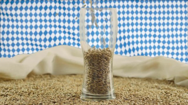 Demonstration of high-quality beer raw materials - malt, malt is poured into a beer glass that stands on a table with laden straw against the background of bilge fabric and a waving Bovar flag