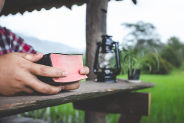 Close up hands holding a red  holy Bible on wood table with green background.