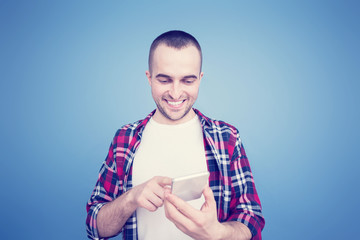 Handsome man, smiling and looks at smartphone screen, front view, blue background, copy space