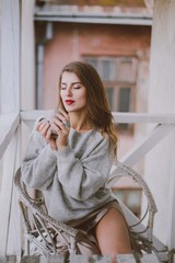 Relaxed woman with cup of coffee or tea. Stylish girl dressed in a gray sweater and silk skirt resting on the balcony.