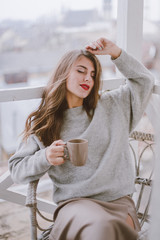 Beautiful young woman enjoying cup of coffee at the balcony 