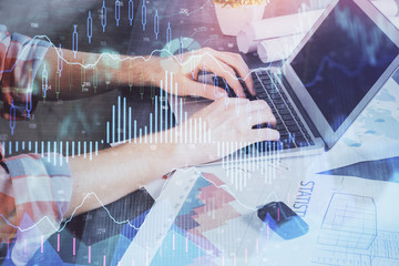 Double exposure of stock graph with businessman typing on computer in office on background. Concept of hard work.