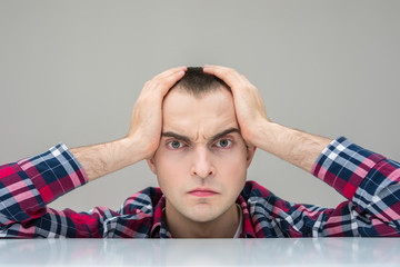 Portrait, a gloomy man looks at the camera, clutching your head, grey background, copy space