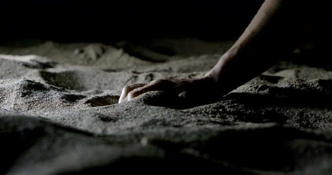 human hand in anger blow to the sand in the dark on the beach at night, close-up