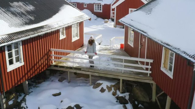 girl standing next to the traditional multicolored wooden fishing house rorbu on a sea shore at Lofoten archipelago, nothern Norway