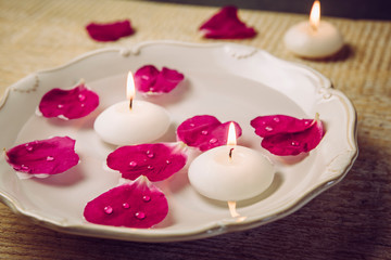 Rose hip( Rosa rugosa, beach rose, Japanese rose) petals floating in water with spa candles, beauty rose water concept.