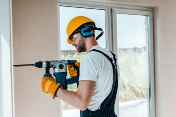 handyman in helmet and yellow gloves using hammer drill