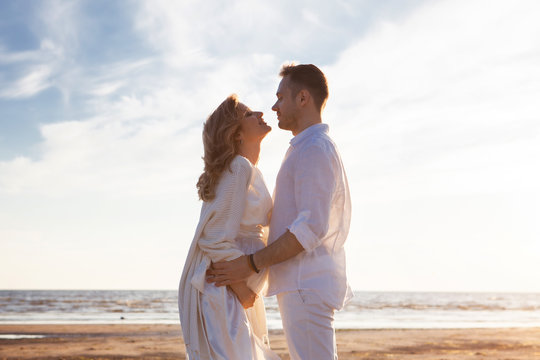 Love, waiting for the baby. Couple, pregnant woman and man, in white flying clothes, walk, hold hands, hug the tummy.